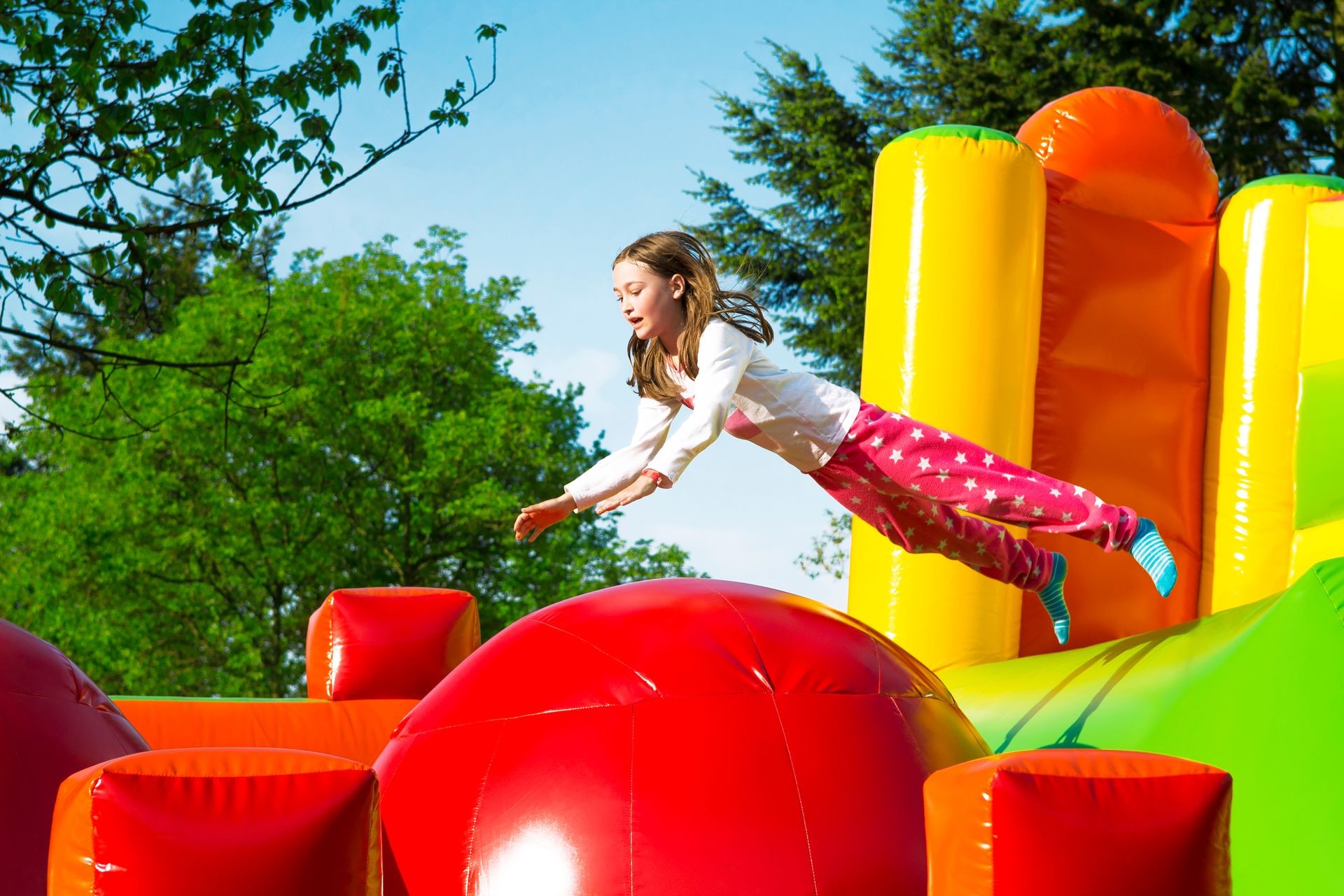 Happy little girl having lots of fun while jumping from ball to ball on an inflate castle.